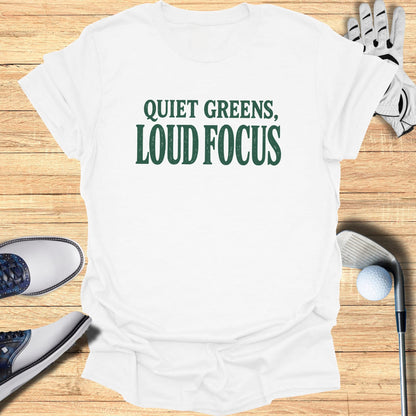 White t-shirt with "QUIET GREENS, LOUD FOCUS" text, golf accessories.