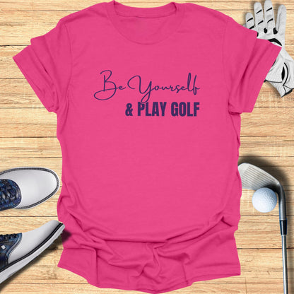 Pink t-shirt with "Be Yourself & Play Golf" text, golf shoes, and club.