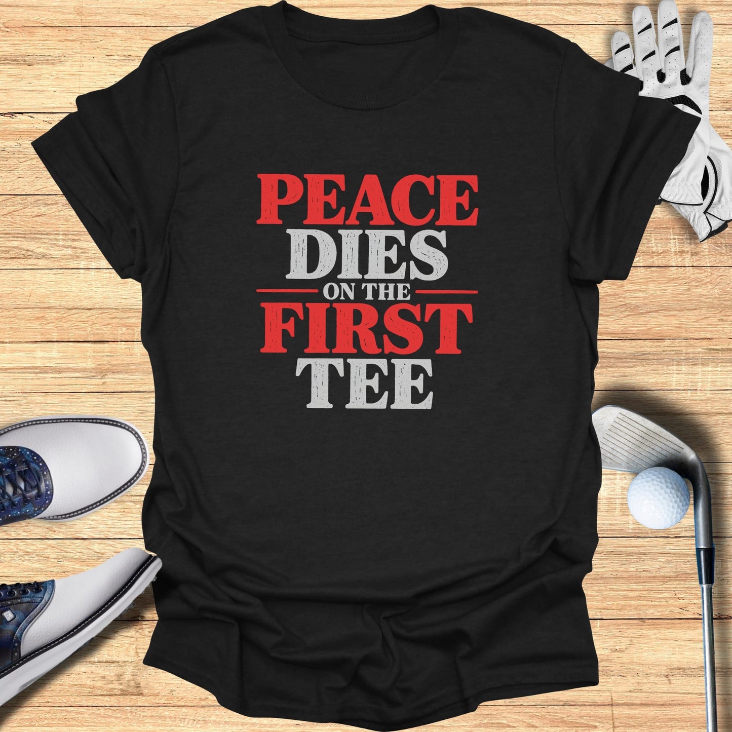 Black t-shirt with "Peace Dies on the First Tee" text and golf accessories.
