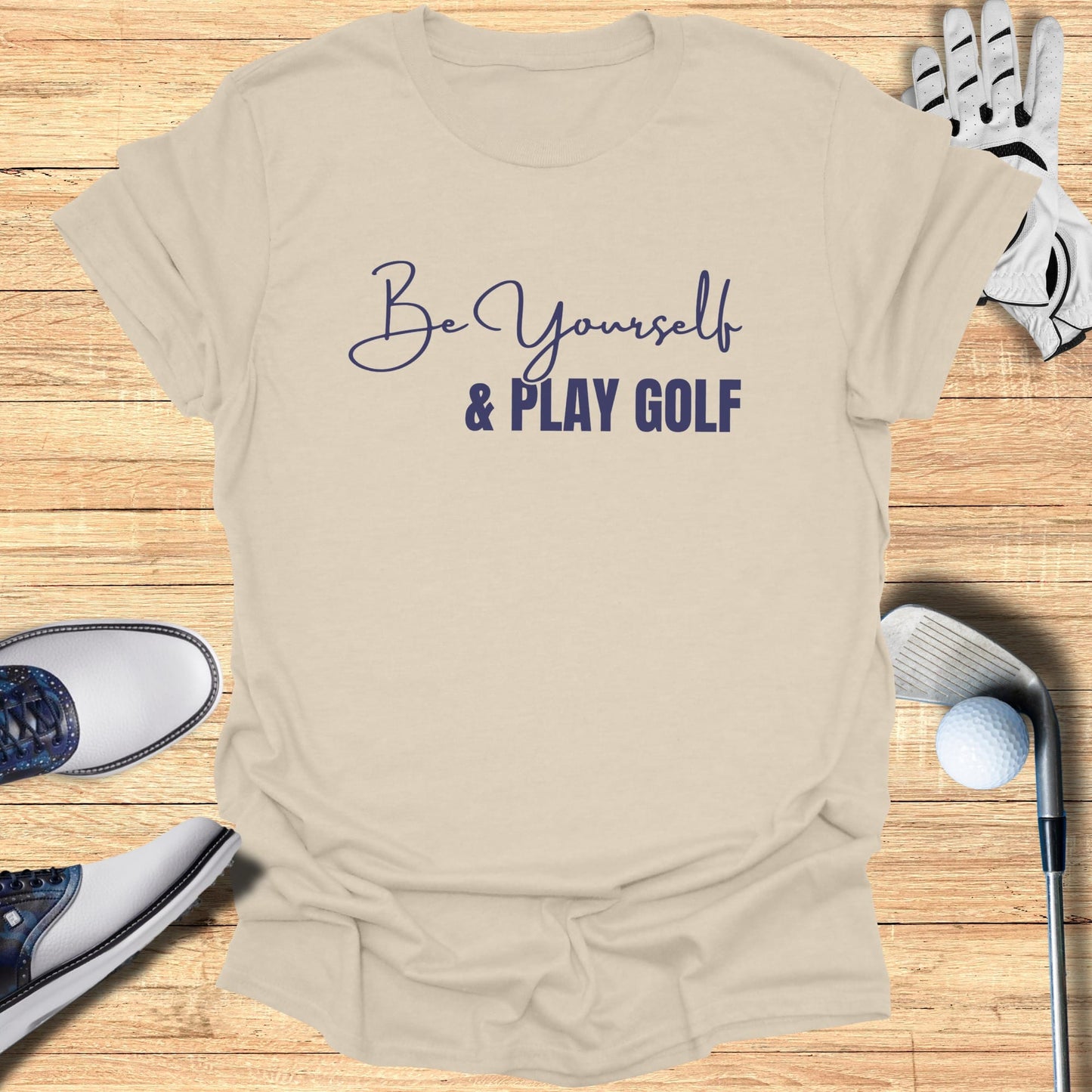 Be Yourself & Play Golf text on a cream t-shirt with golf equipment.