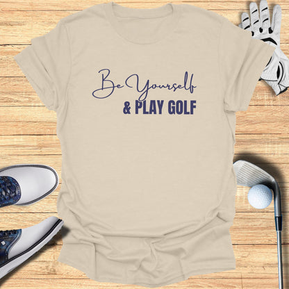 Be Yourself & Play Golf text on a cream t-shirt with golf equipment.