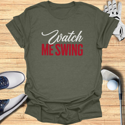 Olive green t-shirt with "Watch ME SWING" text, golf shoes, glove, and club.