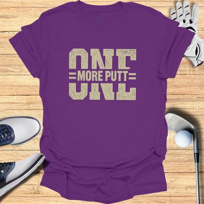 Purple t-shirt with "ONE MORE PUTT" text on a wooden surface.