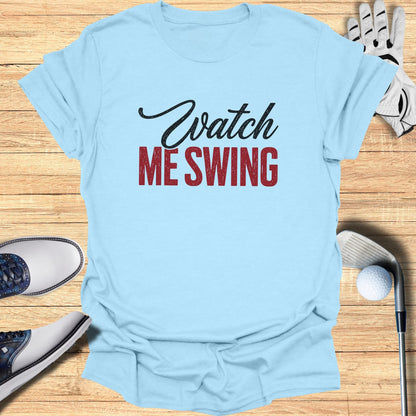 Light blue t-shirt with "Watch ME Swing" text, golf clubs, ball, and shoes.