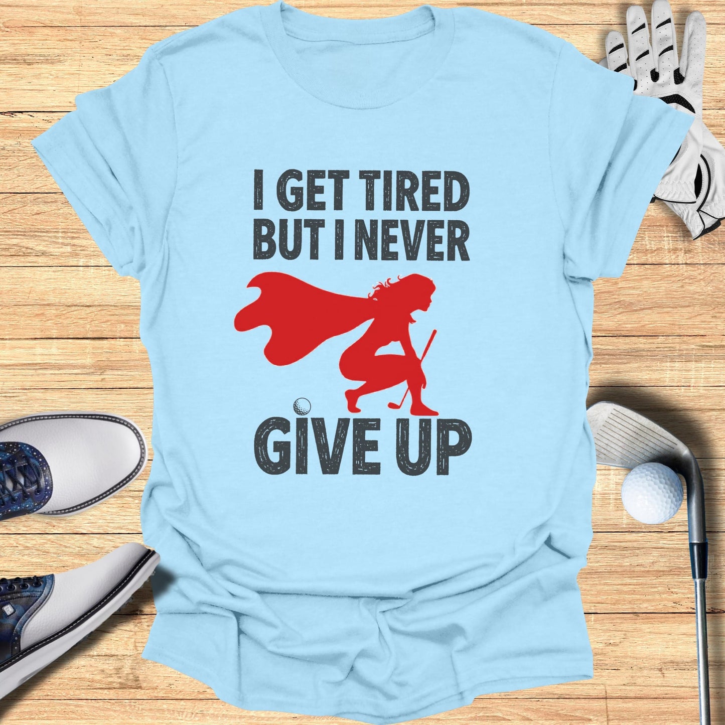 Light blue t-shirt with "I GET TIRED BUT I NEVER GIVE UP" and a superhero golfer graphic.