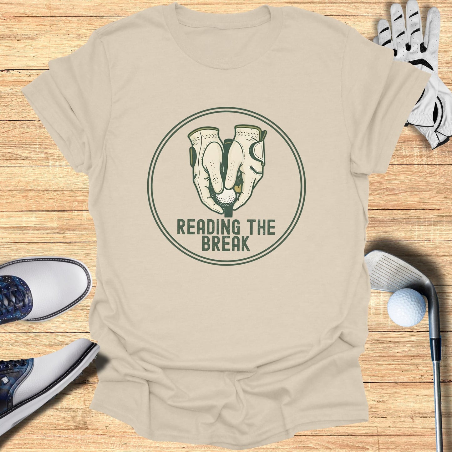 Golf gloves and balls on a beige t-shirt with "READING THE BREAK" text.