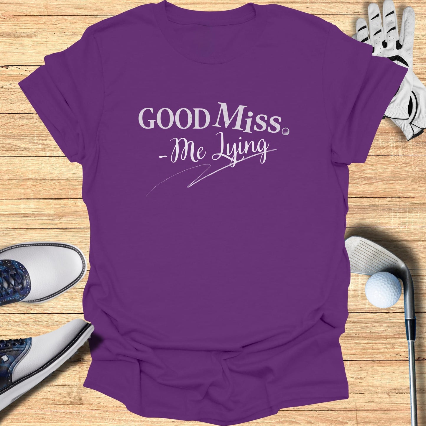 Purple t-shirt with "GOOD Miss. -Me Lying" text, golf club and ball.