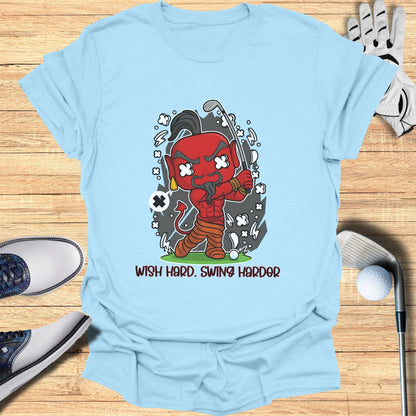 Light blue t-shirt with cartoon devil playing golf and text "Wish Hard. Swing Harder."