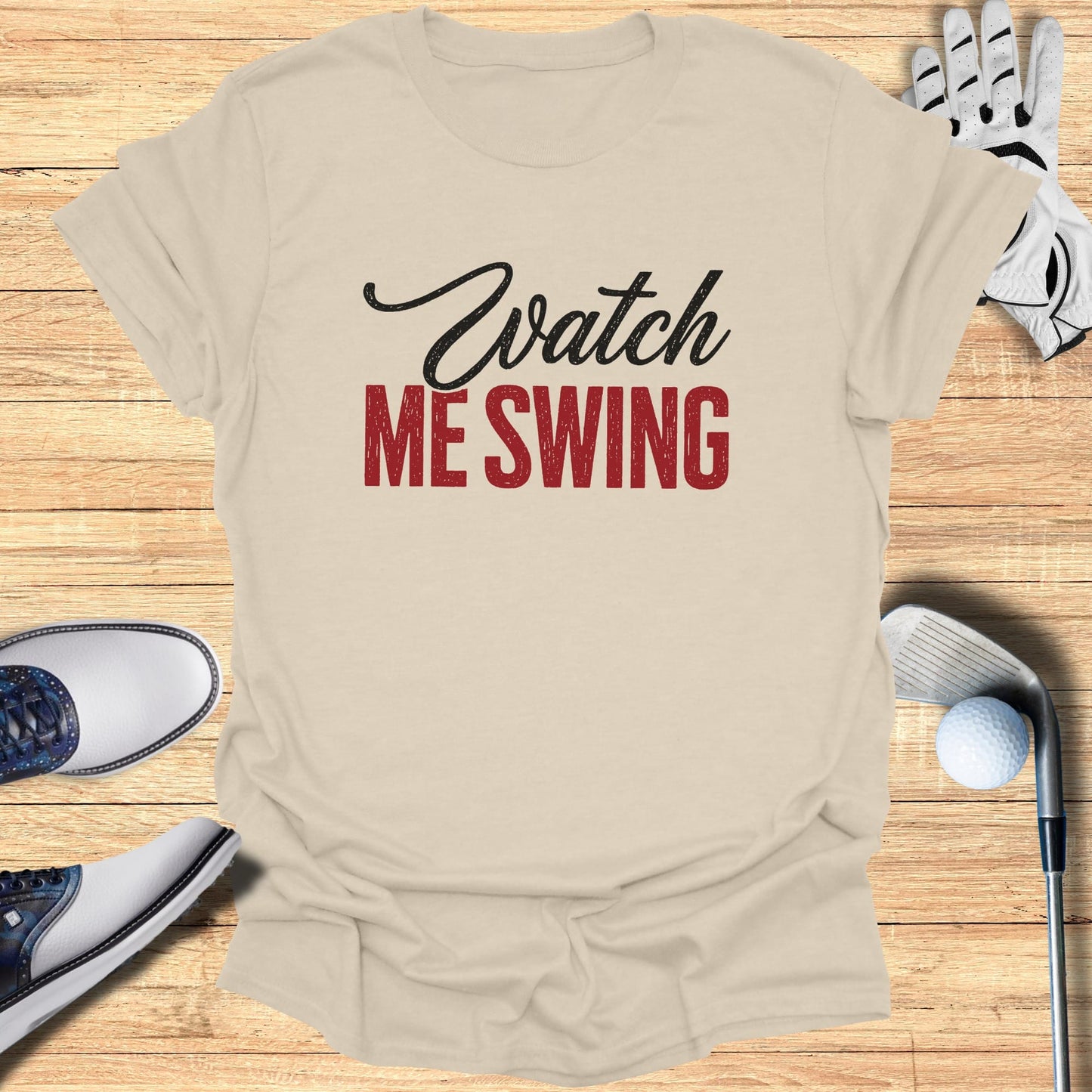 Beige t-shirt with "Watch ME Swing" text, surrounded by golf accessories.