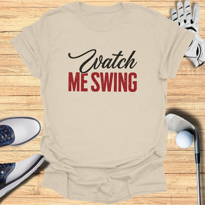 Beige t-shirt with "Watch ME Swing" text, surrounded by golf accessories.