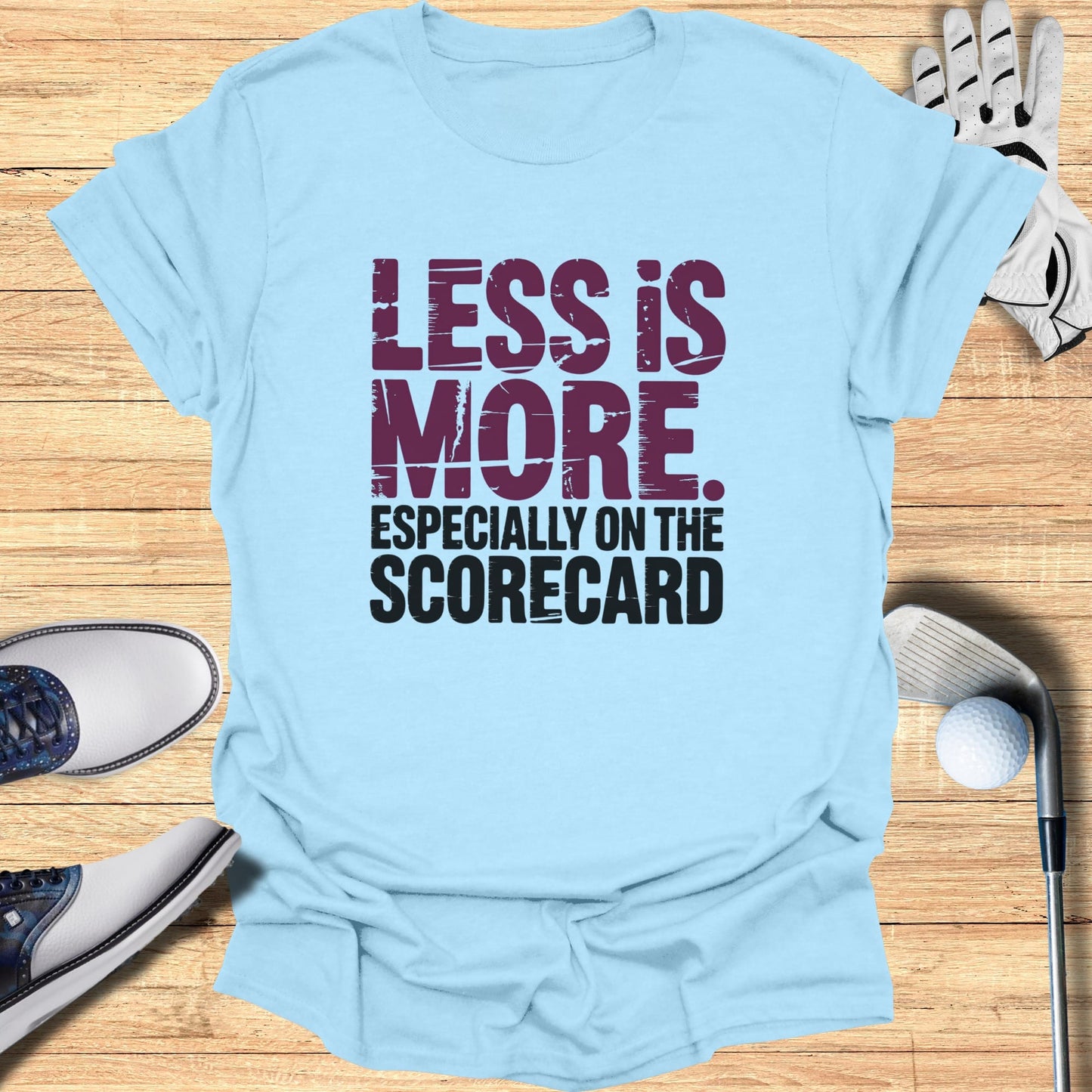 Light blue t-shirt with "LESS IS MORE. ESPECIALLY ON THE SCORECARD." text.