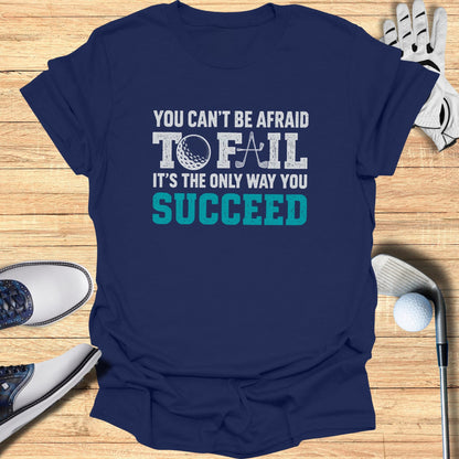 Navy t-shirt with "You can't be afraid to fail" text and golf accessories.