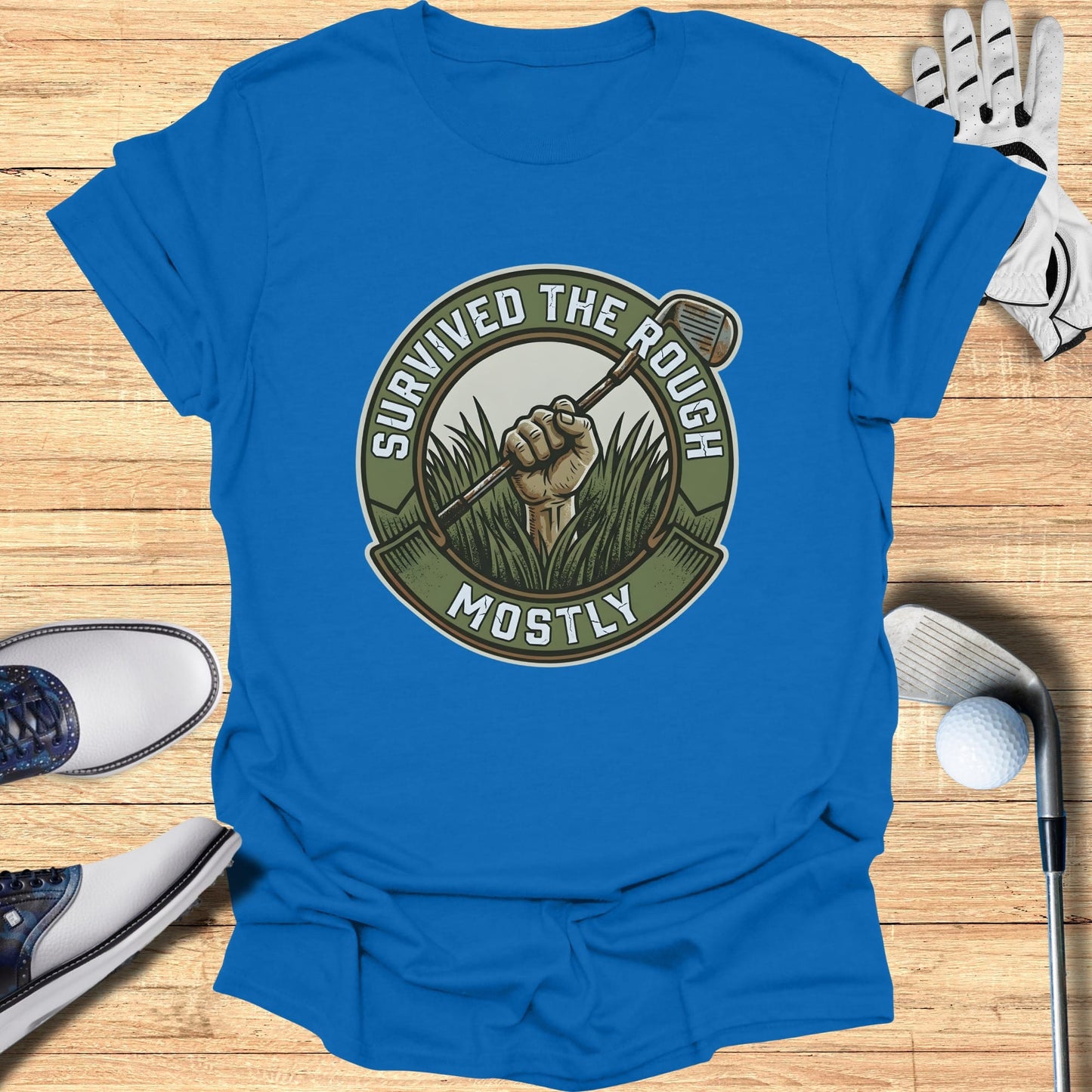 Blue t-shirt with circular graphic of a golf club in grass, text "SURVIVED THE ROUGH MOSTLY".