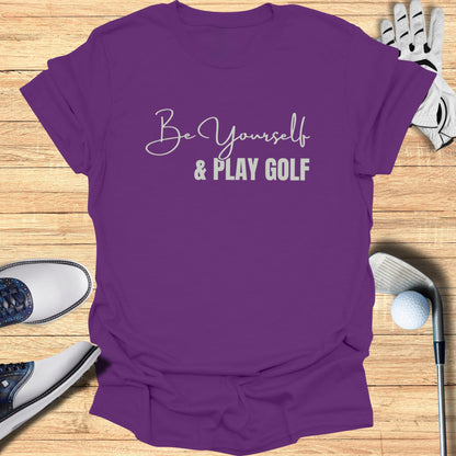 Purple t-shirt with "Be Yourself & Play Golf" text, golf shoes, glove, and club.