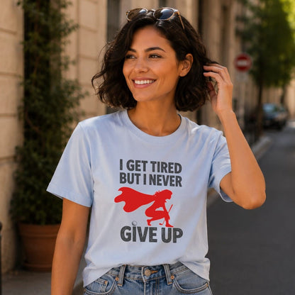 Woman in light blue t-shirt with "I GET TIRED BUT I NEVER GIVE UP" text and superhero graphic.