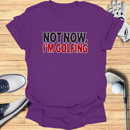 Purple t-shirt with "NOT NOW, I'M GOLFING" text, surrounded by golf shoes and a club.