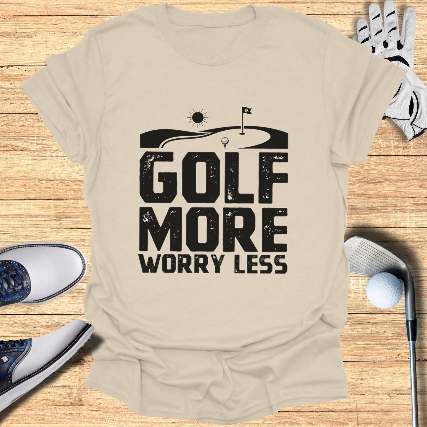 GOLF MORE WORRY LESS text graphic on a beige t-shirt with golf accessories.