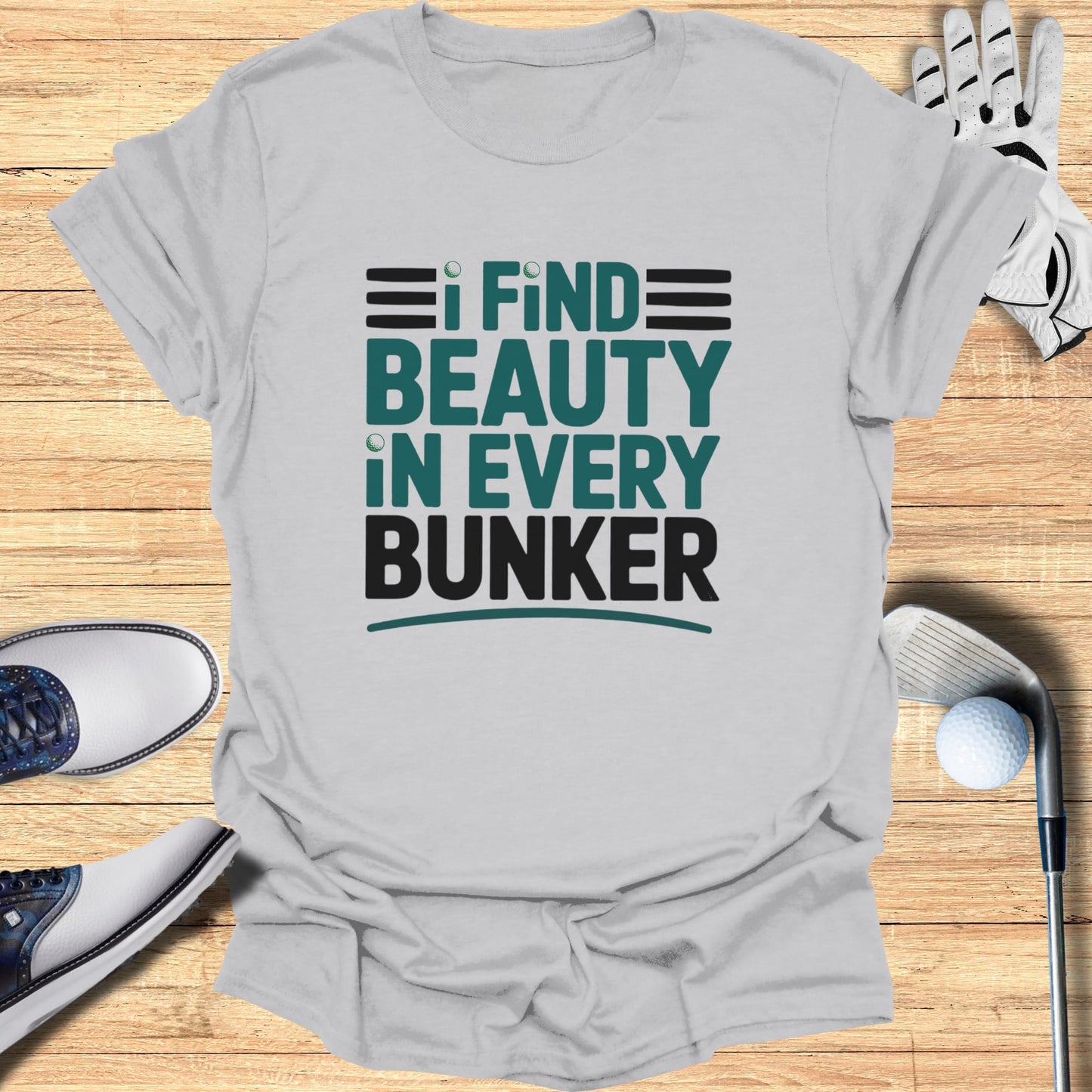 Grey t-shirt with "I FIND BEAUTY IN EVERY BUNKER" text, golf shoes, and golf ball.