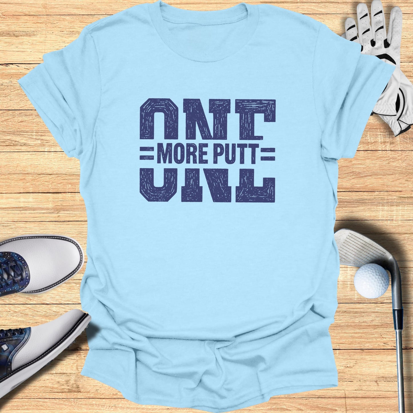 Light blue t-shirt with "ONE MORE PUTT" graphic, golf shoes, glove, and ball.